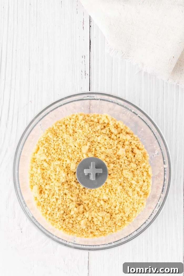 A close-up of finely crumbled golden Oreo cookies, showcasing their uniform texture, ready to be mixed with butter for the cheesecake crust.