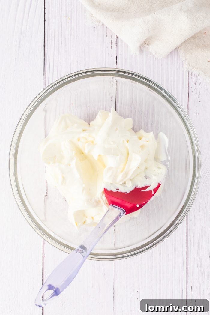 Softened cream cheese, perfectly smooth and ready to be mixed, sits invitingly in a clear glass bowl, glistening under the light.