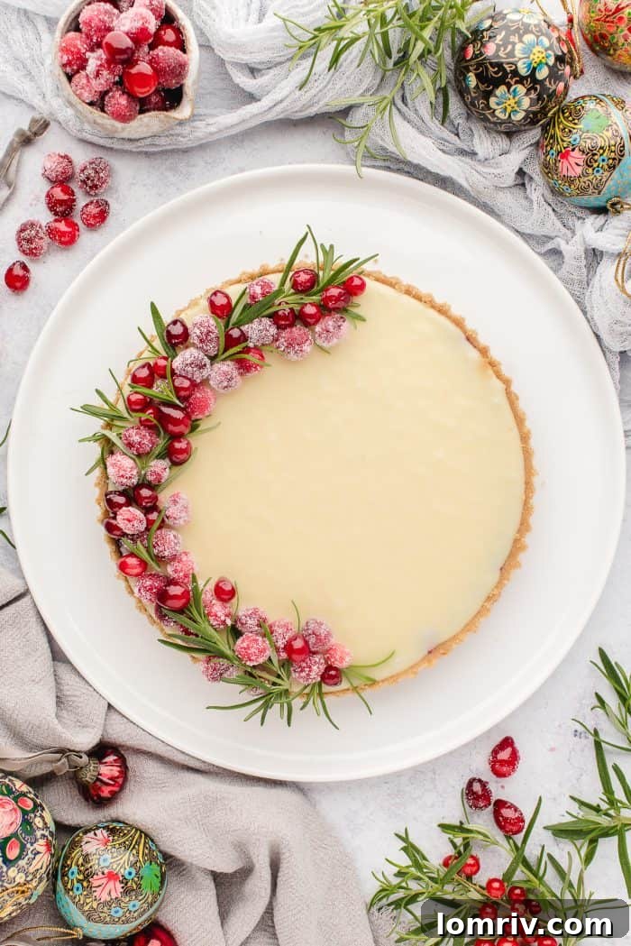 A beautifully garnished white chocolate cranberry tart viewed from overhead, surrounded by fresh rosemary and cranberries.
