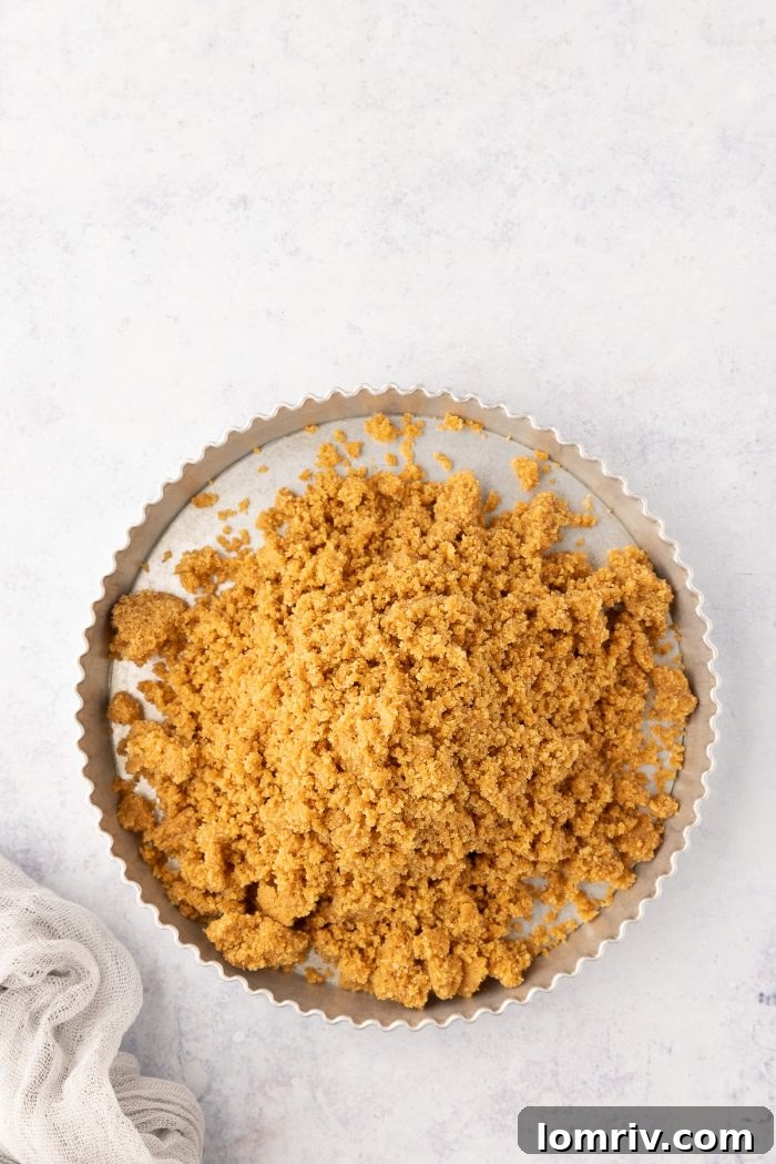 The graham cracker crumb mixture being carefully transferred into a tart pan.