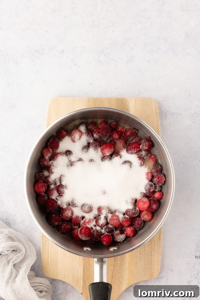 Fresh cranberries, sugar, and orange juice simmering in a saucepan for the cranberry layer.