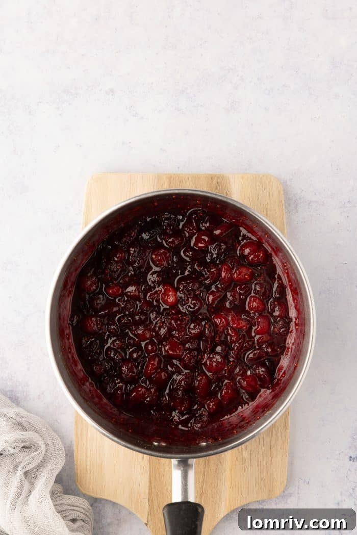 The cooked cranberry jam, thick and vibrant, cooling in a saucepan.