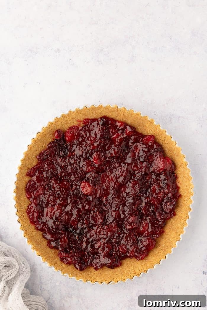 The vibrant cranberry jam being spread into the graham cracker crust.