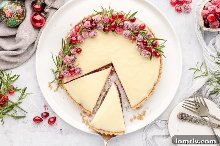 An inviting overhead photograph of a white chocolate cranberry tart on a white plate, with two slices cut out.