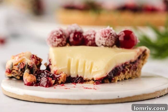 A close-up view of a slice of the white chocolate cranberry tart on a white plate, showing its layers.