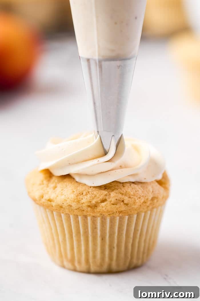 Piping whipped brown butter buttercream onto a cooled peach cupcake
