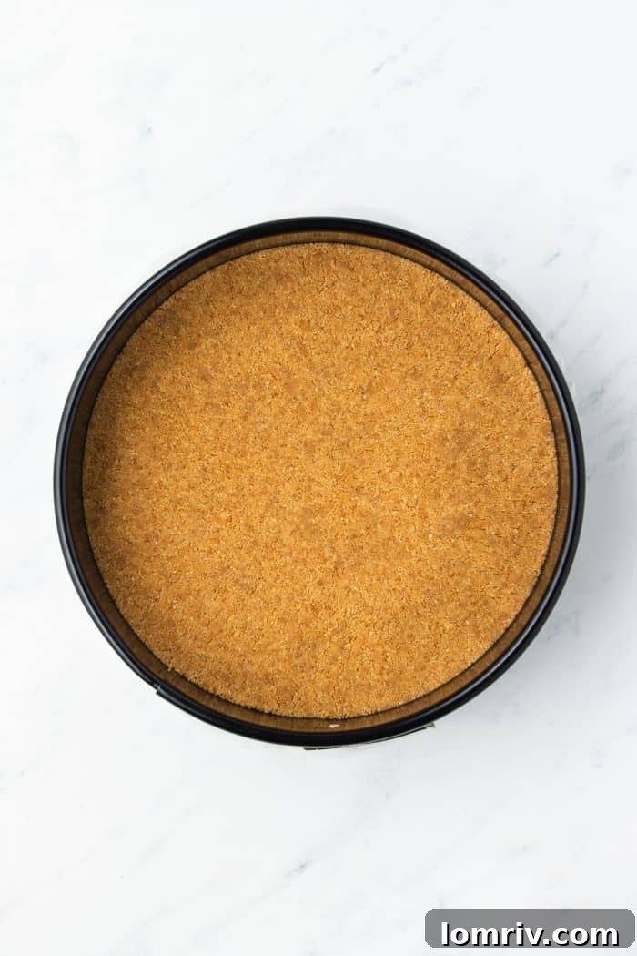 The buttery graham cracker crust meticulously pressed into the base of a springform pan, forming a solid, even layer.