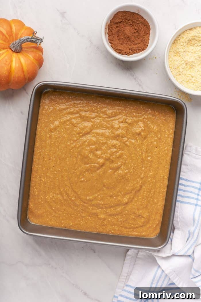 A baking pan filled with raw pumpkin cornbread batter with a small pumpkin and bowls of ingredients.