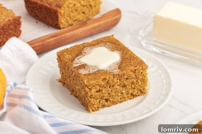 A slice of pumpkin cornbread with melted butter on a white plate.