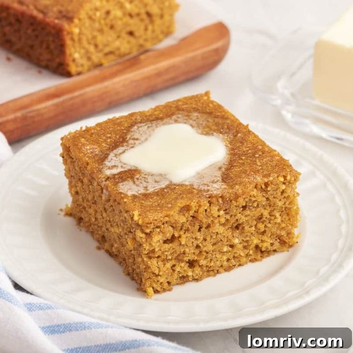 A slice of pumpkin cornbread with melted butter on a white plate.