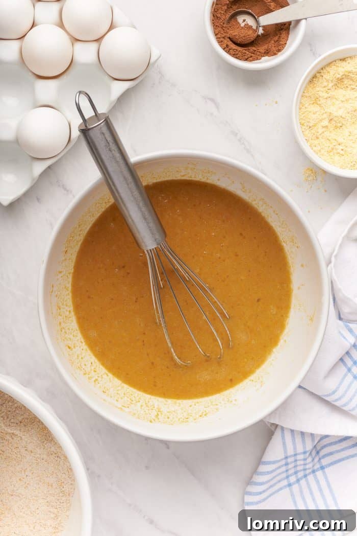 A white bowl with the pumpkin puree mixed with eggs and a whisk.