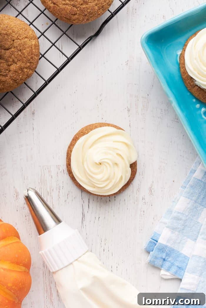Pumpkin snickerdoodle cookies with cream cheese frosting and cookies in the background on a cooling rack with a bag of frosting.