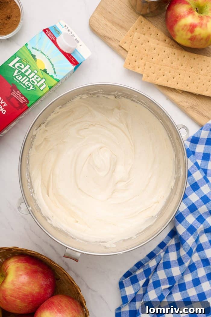 A bowl showing cream cheese and heavy cream beautifully mixed together, forming a smooth and thick cheesecake filling.