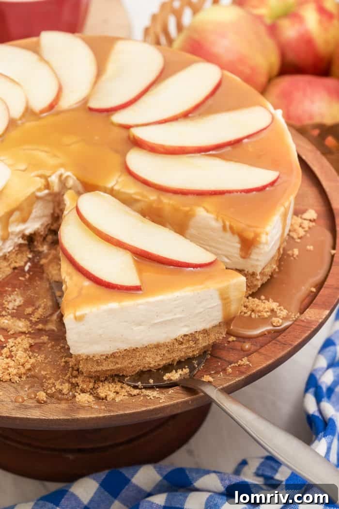 A slice of apple caramel cheesecake being removed from the whole cheesecake, revealing its creamy layers and graham cracker crust.