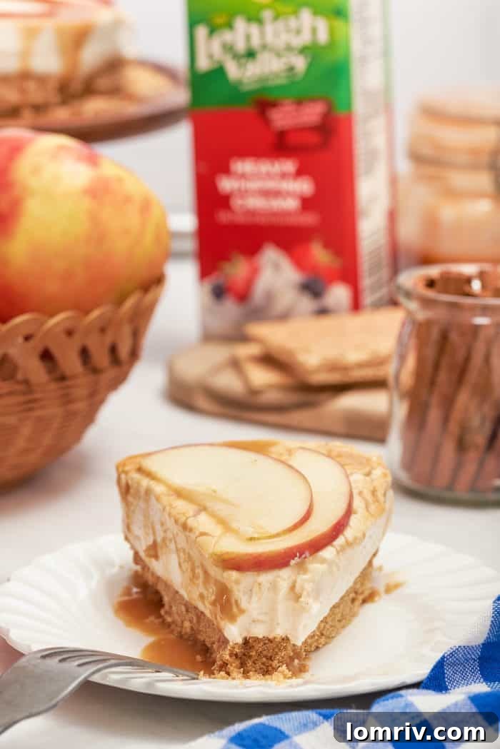 A close-up of a slice of apple cheesecake on a white plate, with a carton of heavy whipping cream in the background, implying its creamy texture.