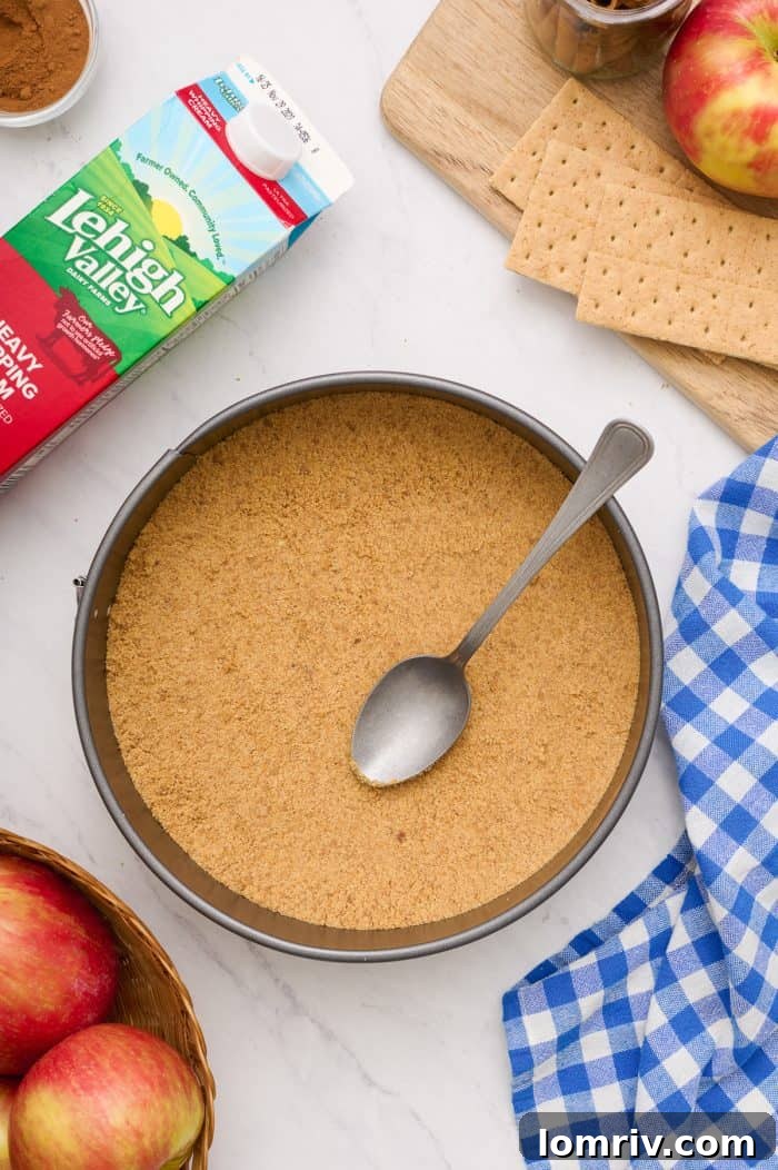A cheesecake pan with the graham cracker crumbs neatly pressed into the base, smoothed out with a spoon.