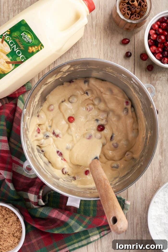 Fresh cranberries gently folded into the coffee cake batter in a mixing bowl, ensuring even distribution for bursts of tartness in every bite.