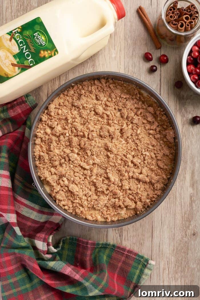 The unbaked cranberry eggnog coffee cake, complete with its generous streusel topping, nestled in a round cake pan, ready for the oven.