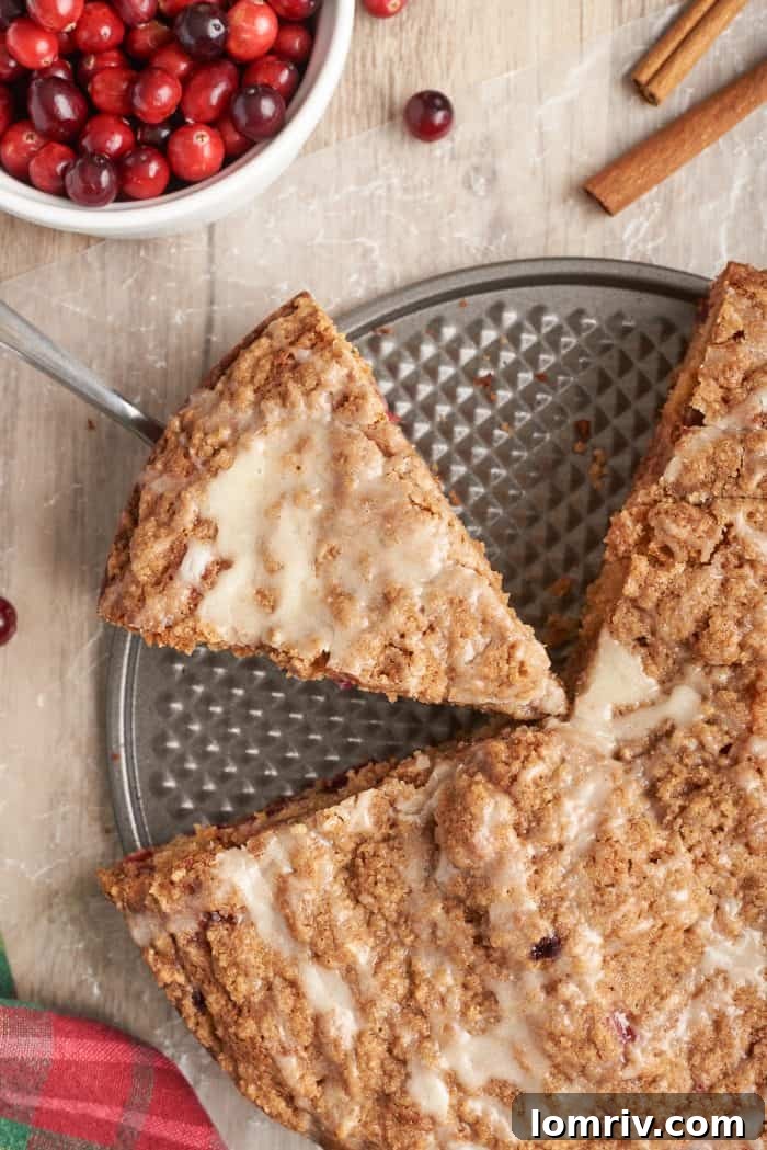 A slice of cranberry eggnog coffee cake being carefully removed from the springform pan, showcasing its moist interior and crumble topping.