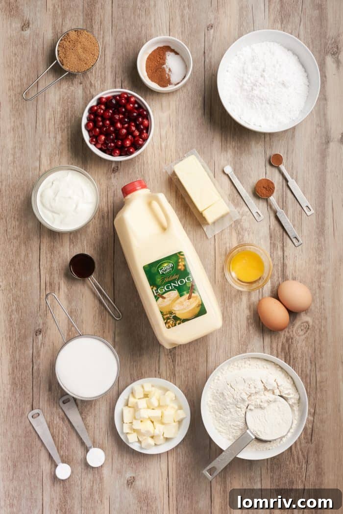 An organized flat lay of all the essential ingredients for making cranberry eggnog coffee cake, including flour, spices, butter, eggs, cranberries, and eggnog.