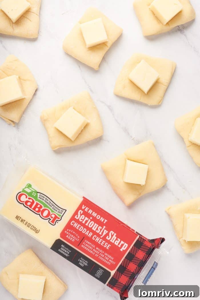 A spread of dough squares, each with a cube of cheese nestled in the center, ready to be folded and rolled into cheesy bread balls.