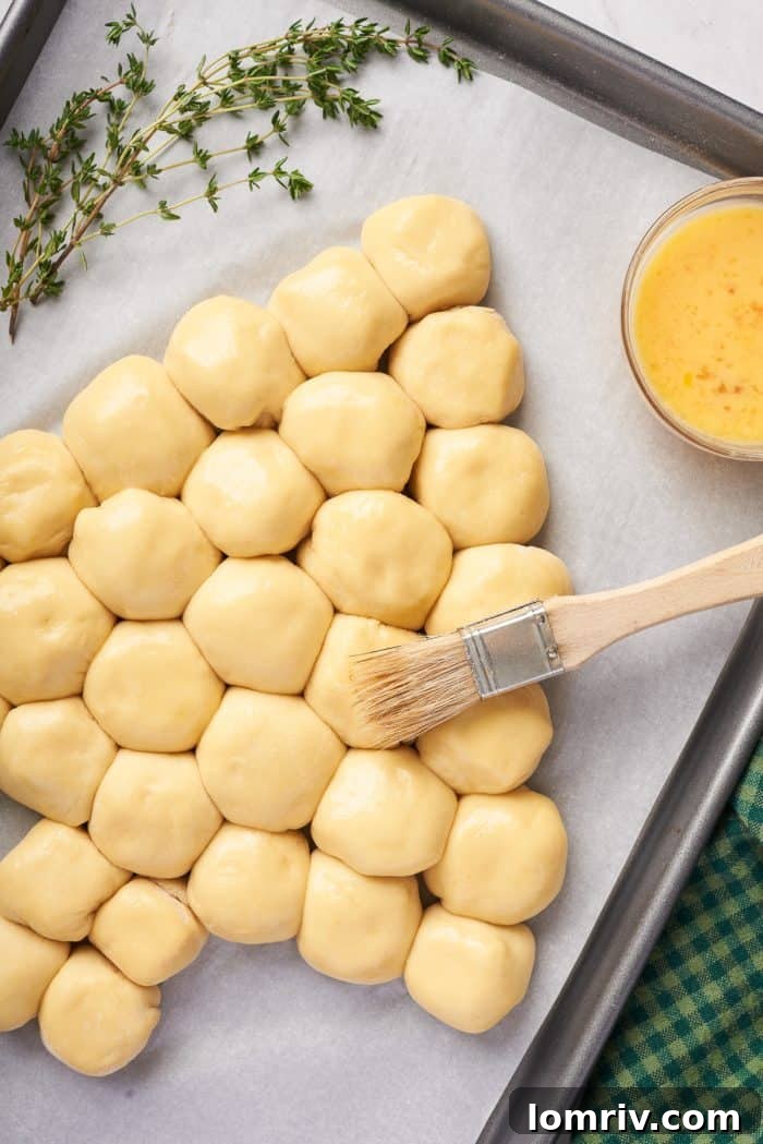 A pastry brush expertly applies egg wash to the top of the Christmas tree dough balls, preparing them for a golden crust.