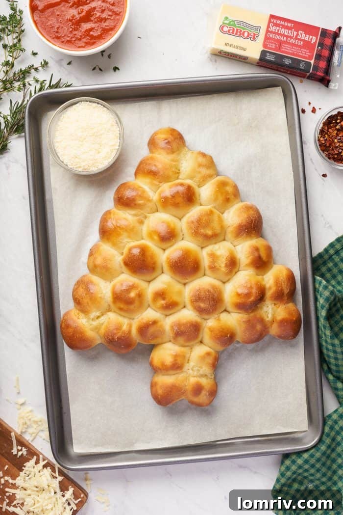 The freshly baked pull-apart Christmas tree bread, glistening with a golden hue, sits proudly on its baking sheet.