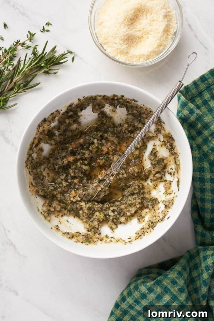 A white bowl holds the vibrant mixture of melted butter, herbs, and spices, ready to be brushed onto the warm bread.
