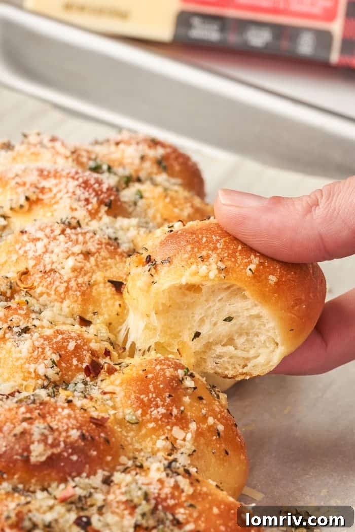 A hand gently pulls a piece of the cheesy Christmas tree bread from the main loaf, revealing its soft interior.