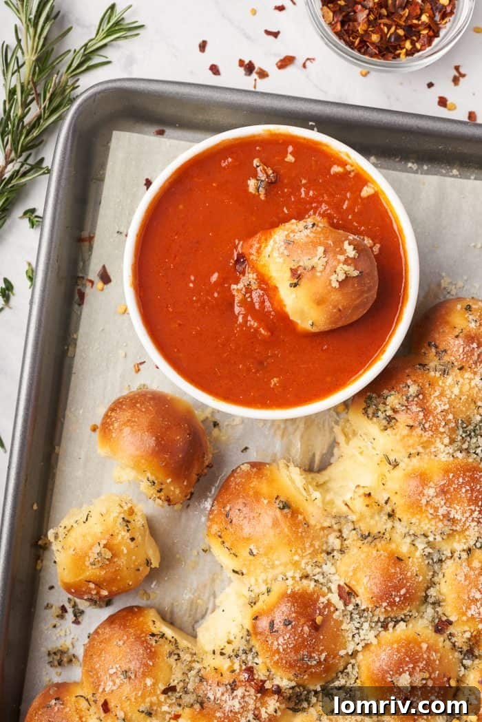 A single piece of the cheesy pull-apart bread, perfectly detached and dipped into a small bowl of marinara sauce, inviting a delicious bite.