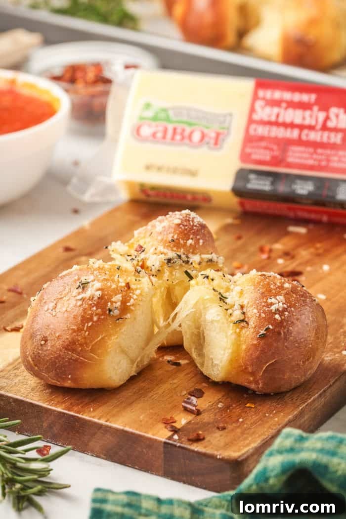Three perfectly formed dough balls, ready for baking, sit on a wooden cutting board with a block of sharp cheddar cheese in the background.
