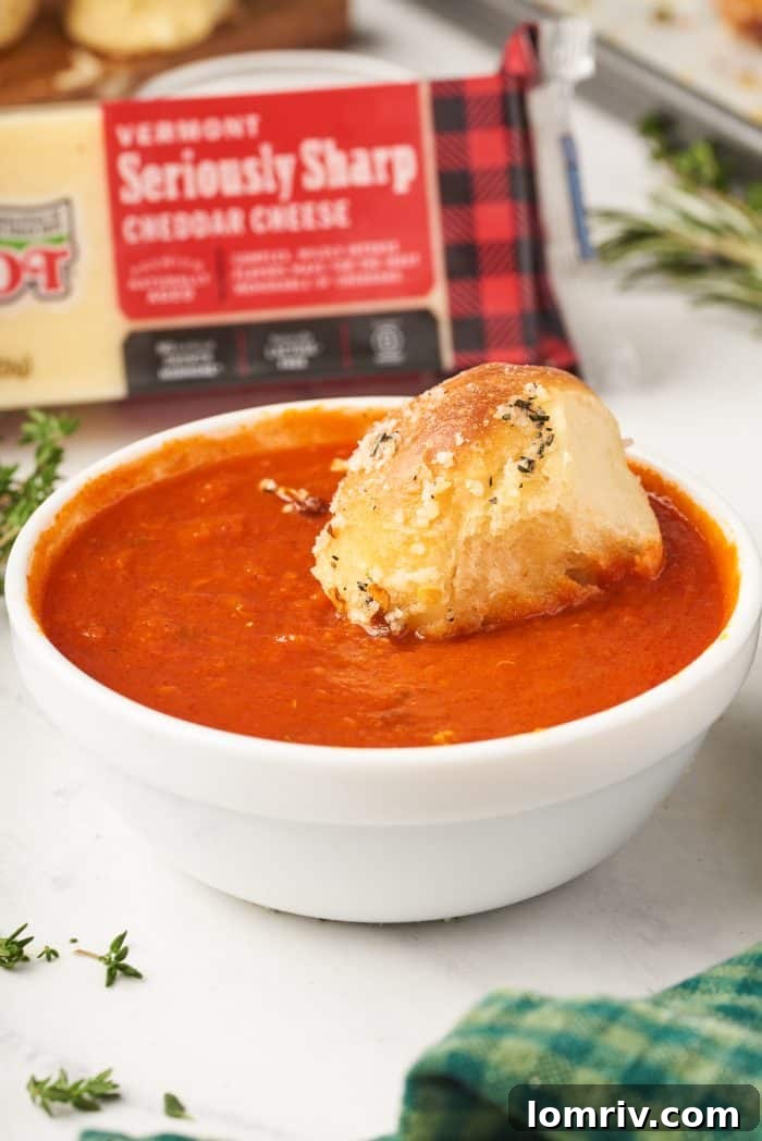 A baked, cheesy bread ball from the Christmas tree loaf, perfectly dipped in a bowl of vibrant marinara sauce, ready to be enjoyed.