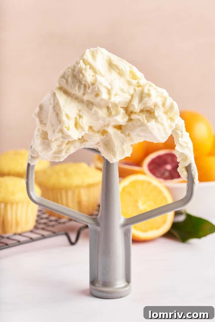 Silky, orange-infused Swiss meringue buttercream cascading off a whisk attachment, showcasing its smooth, luxurious texture.