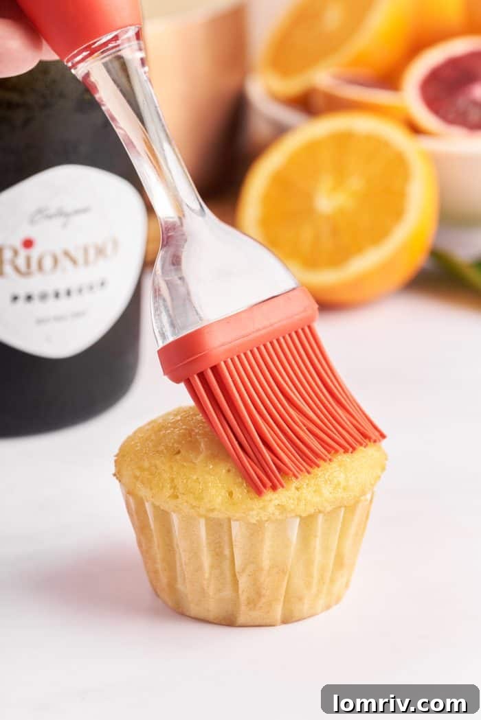 A hand gently brushes a baked cupcake with glistening Prosecco syrup, demonstrating the infusion process for enhanced flavor.