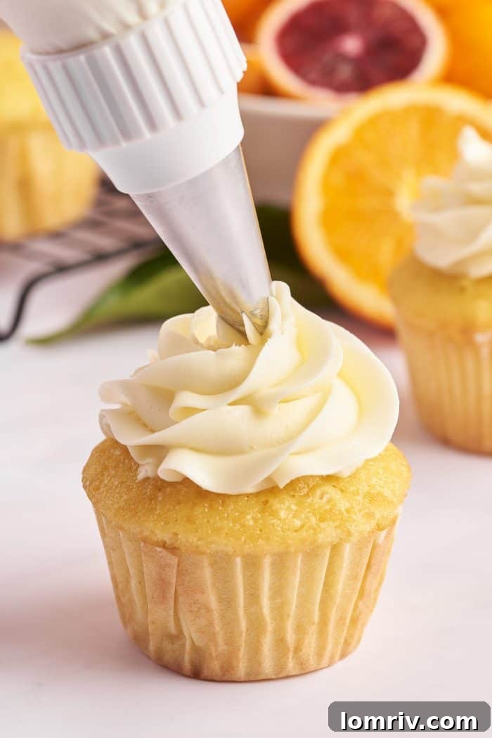 A mimosa cupcake is in the process of being frosted with a generous swirl of orange buttercream, demonstrating the final step in its creation.