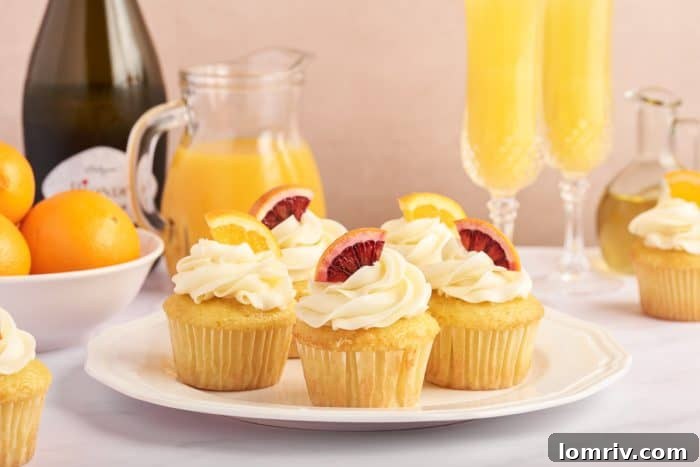 A visually appealing spread features a white plate laden with an assortment of mimosa cupcakes, each distinctively frosted and garnished. In the background, bottles of Prosecco and orange juice, alongside two glasses of mimosas, complete the inviting brunch scene.