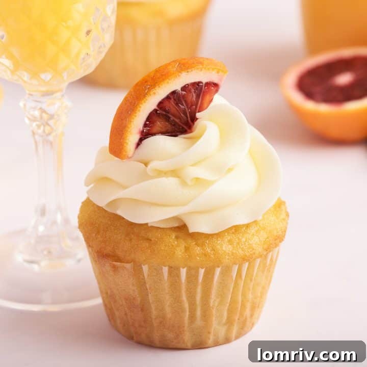 A mimosa cupcake with a glass of mimosa and a glass bottle of orange juice in the background.