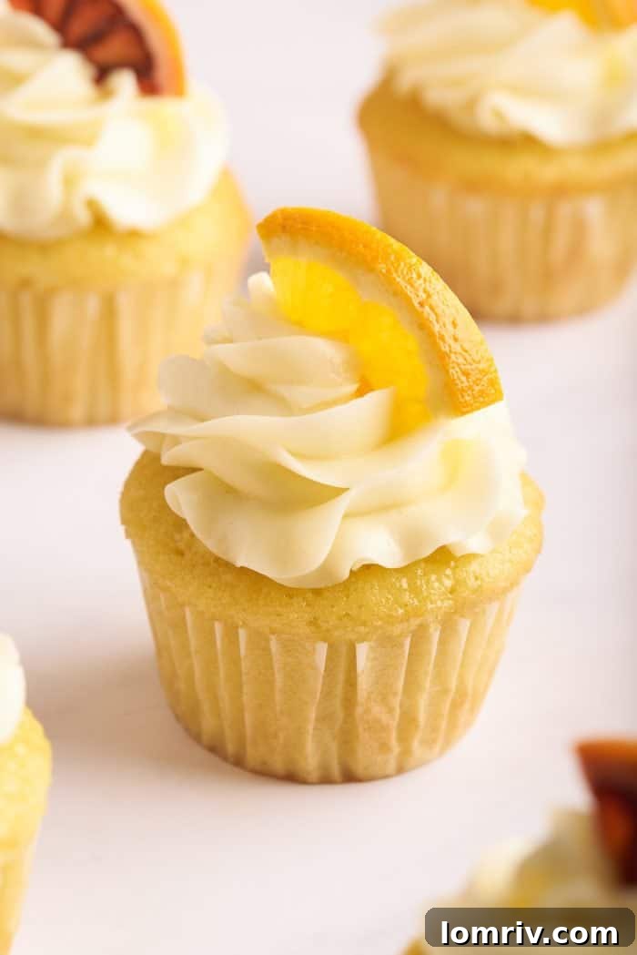 A close-up shot of several mimosa cupcakes, each topped with creamy, orange-infused buttercream and garnished with a fresh orange slice, showcasing their vibrant appeal.
