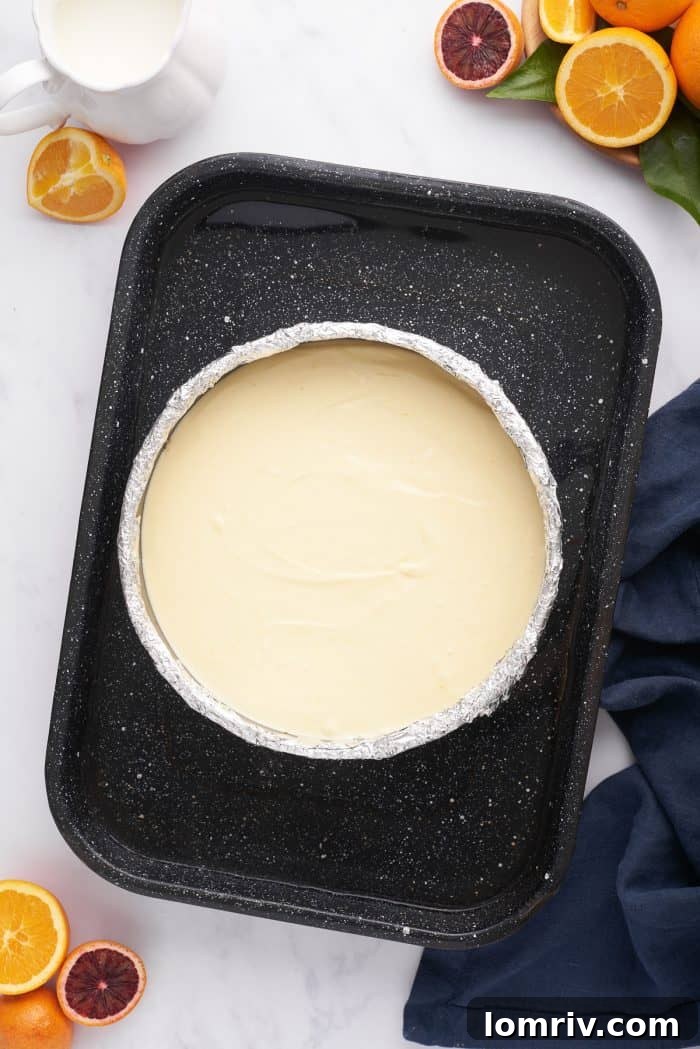 The unbaked cheesecake in its springform pan, nestled inside a larger baking pan filled with water, ready for the oven.