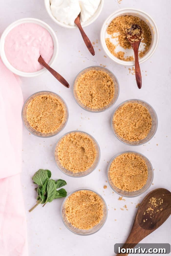 Graham cracker crust being pressed into 6 individual glass jars.