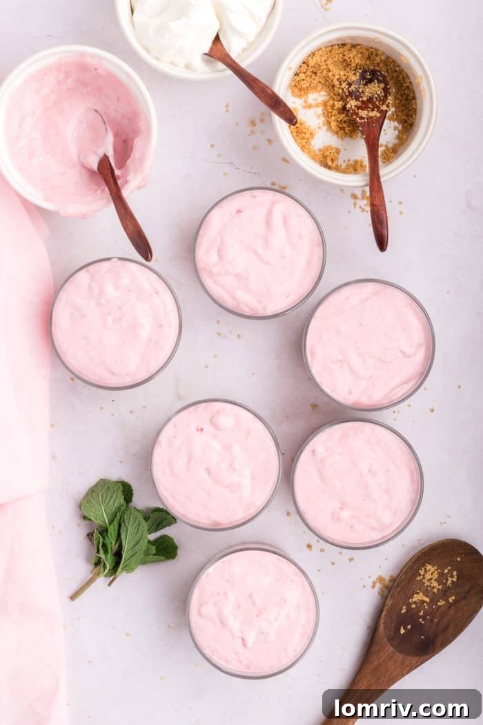 Raspberry mousse filling being added to 6 glass serving dishes over the crust.