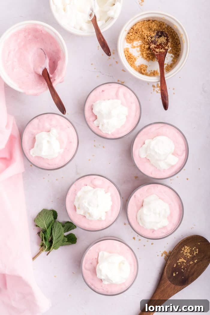 Whipped cream topping being placed on top of the raspberry mousse in serving dishes.