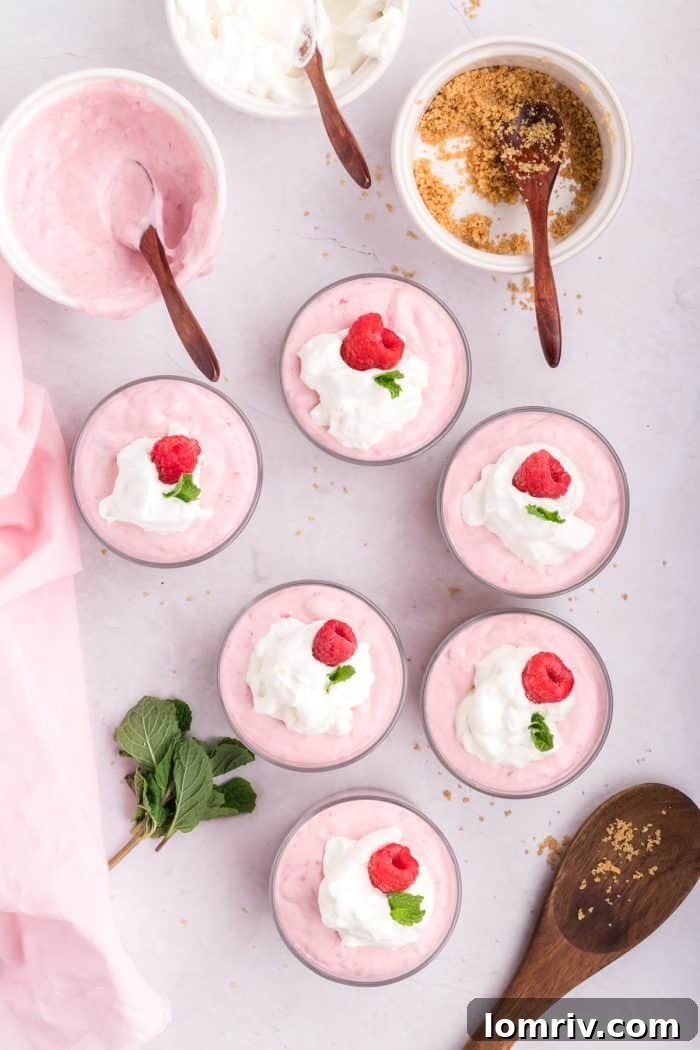 A mint leaf being added as a garnish to each raspberry mousse.
