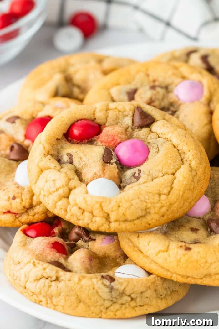 A charming pile of freshly baked Valentine's M&M Cookies, adorned with colorful candies, resting invitingly on a white plate.