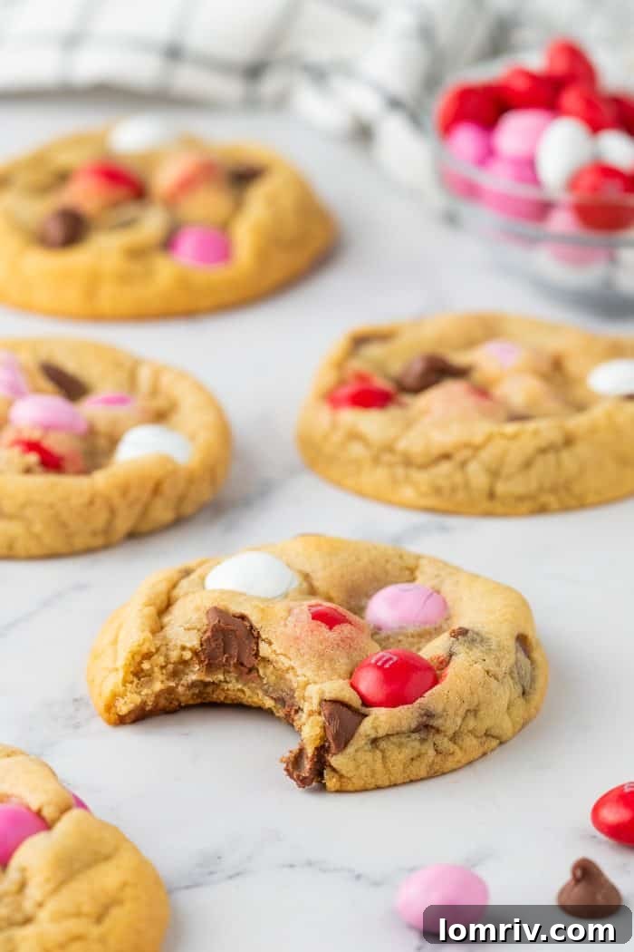 An inviting arrangement of four freshly baked Valentine's M&M cookies, with one showing a bite, beautifully showcasing their festive appeal and deliciousness.