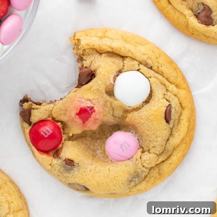 A close up of a Valentine's M&M cookie with a bite out of it and cookies around it.