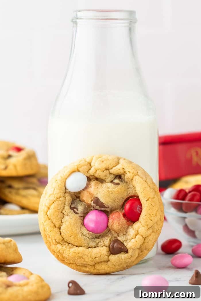 A refreshing glass of milk, perfectly paired with a warm, soft Valentine's M&M cookie, capturing a classic moment of indulgence.