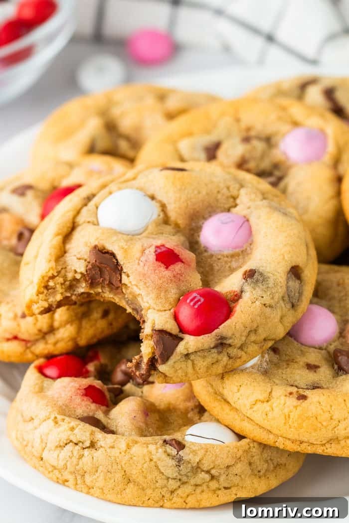 A tantalizing close-up of a Valentine's M&M Cookie with a perfect bite taken out, revealing its soft, chewy interior and the delightful meld of chocolate and colorful candies.
