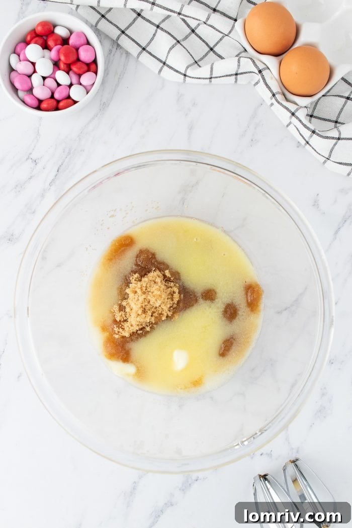 A clear glass mixing bowl holds the perfectly creamed mixture of melted butter, brown sugar, and granulated sugar, displaying a smooth and uniform texture.