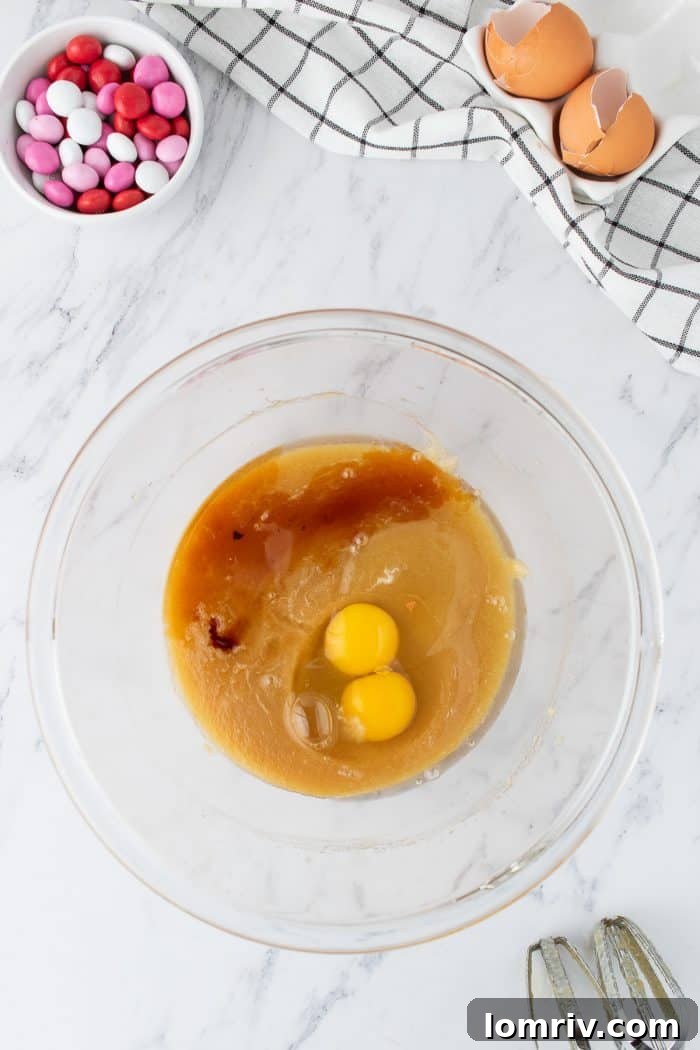 The butter and sugar mixture in a glass bowl, now enriched with two fresh eggs and vanilla extract, ready to be blended into a cohesive wet base.